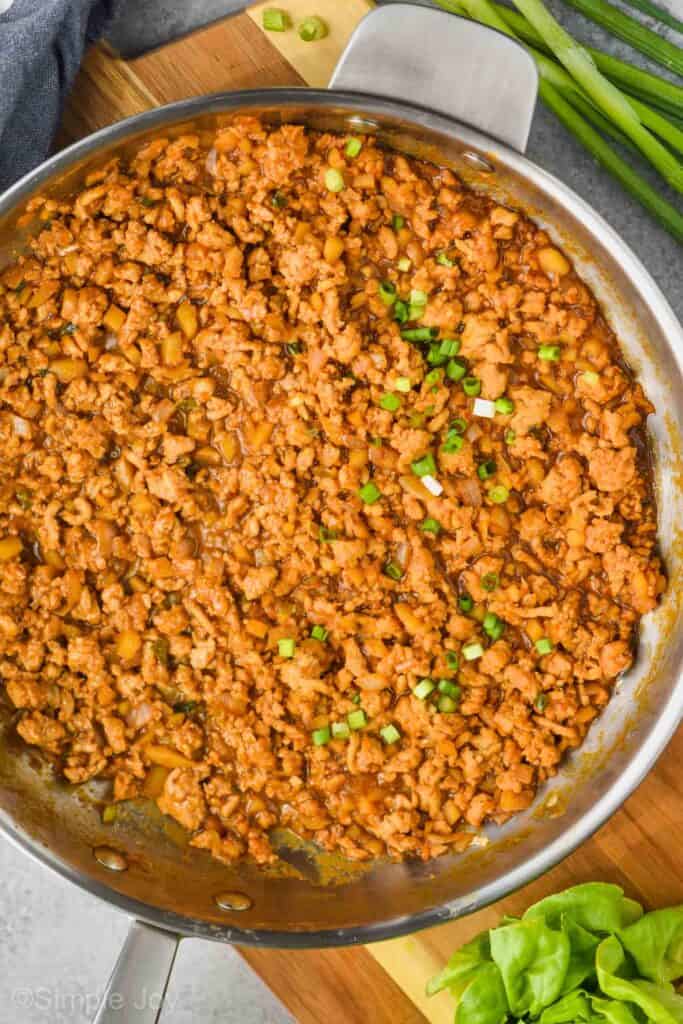 overhead view of a pan with the filling for healthy chicken lettuce wraps garnished with raw diced green onion