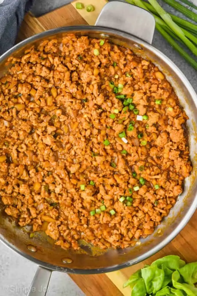 overhead view of a pan with the filling for healthy chicken lettuce wraps garnished with raw diced green onion