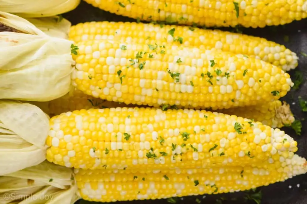 up close view of grilled corn that has had the husks pulled back with fresh parsley and butter