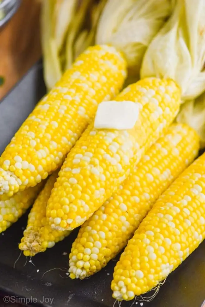 grilled corn with the husks pulled back and a square of butter melting on the cob