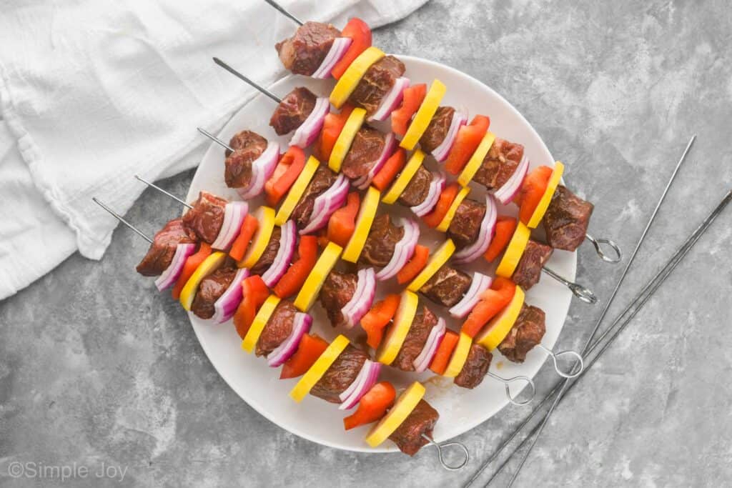 steak kabobs on a white round plate with metal skewers before being cooked