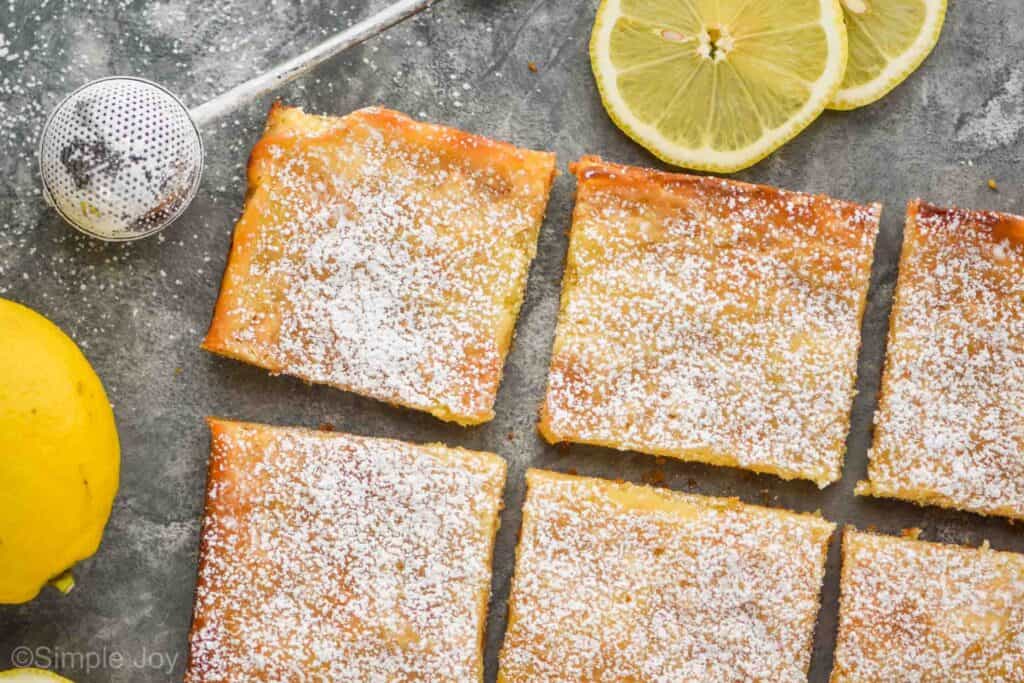 two rows of lemon magic bars from overhead with a powdered sugar wand and two lemon slices and a lemon next to them