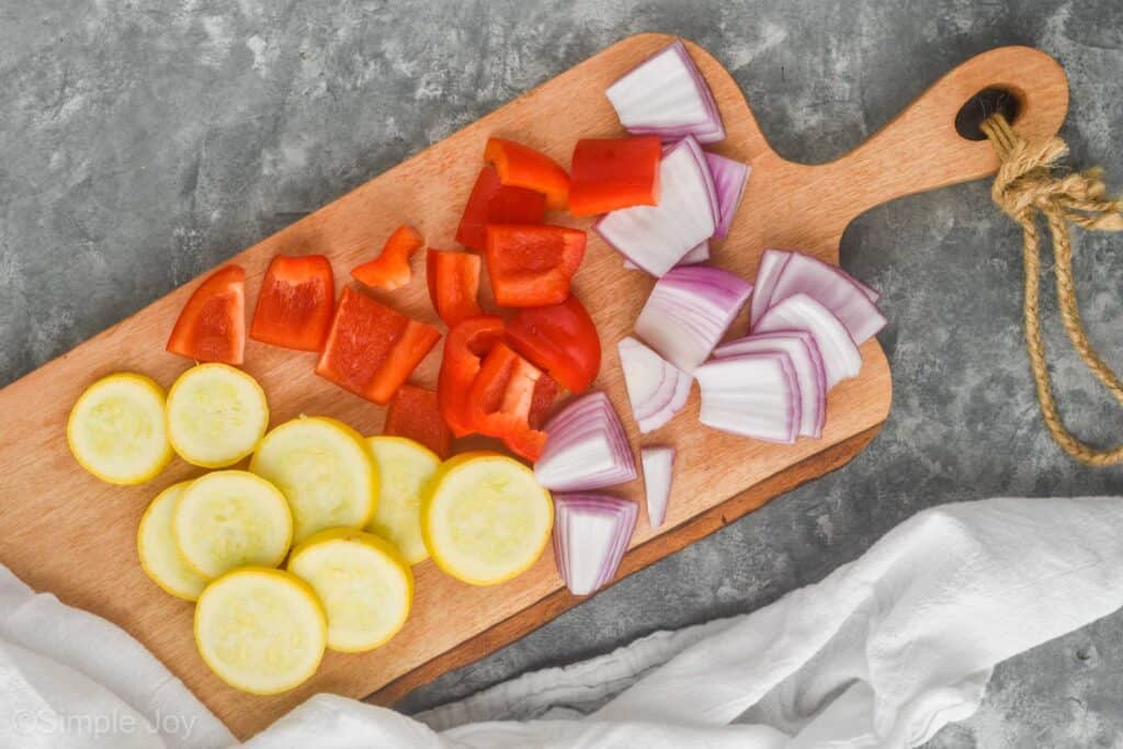 cut up yellow zucchini, red peppers, and red onions on a wood cutting board