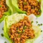 close up of a chicken lettuce wrap garnished with fresh diced green onions on a white plate