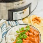 bowl of crockpot butter chicken with naan bread on the side and a slow cooker in the background