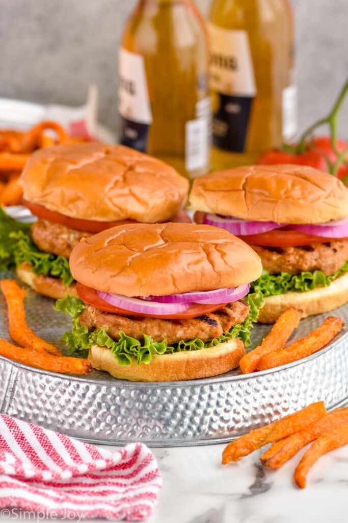 Overhead photo of Turkey Burgers served on buns and garnished with lettuce, tomato, and onion. Fries and bottles of beer sit beside Turkey Burgers.