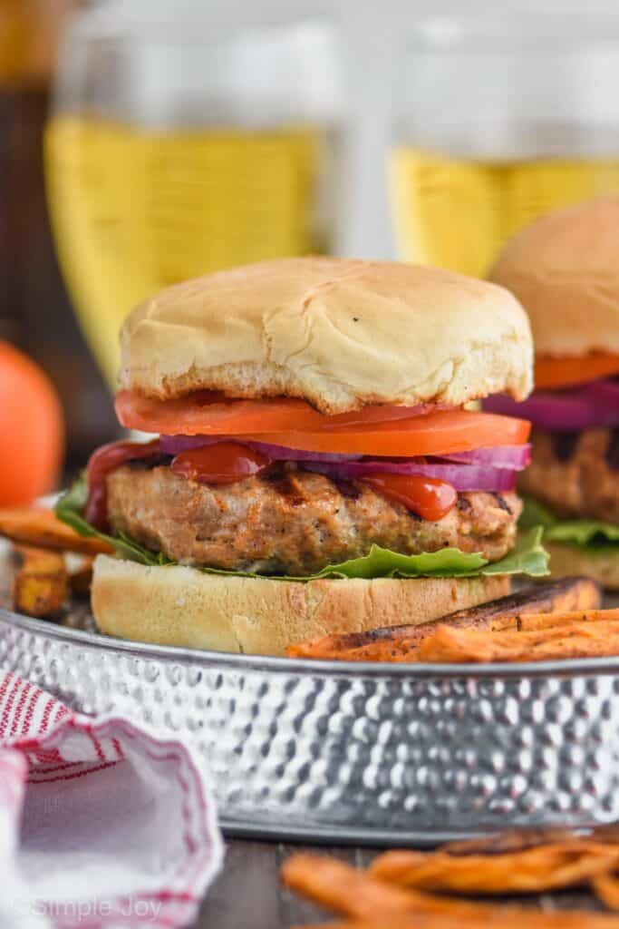 close up of a turkey burger on a bun with lettuce, ketchup, red onion, and tomato with sweet potato fries next to it