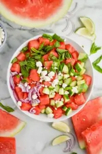 overhead view of watermelon salad broken up by ingredients: watermelon, fresh mint, feta, red onions, and cucumber slices cut into fourths.