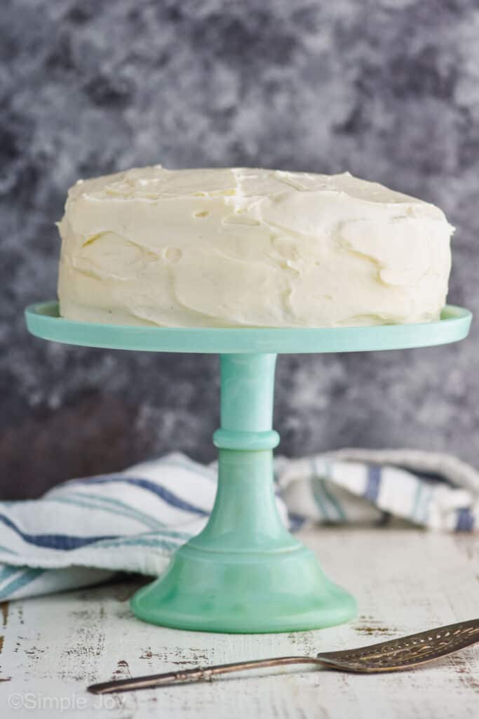 three layer zucchini cake, before being cut, frosted with cream cheese frosting on a teal cake stand