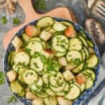 overhead view of a zucchini salad recipe in a bowl on a cutting board, salad is garnished with more fresh herbs - 5