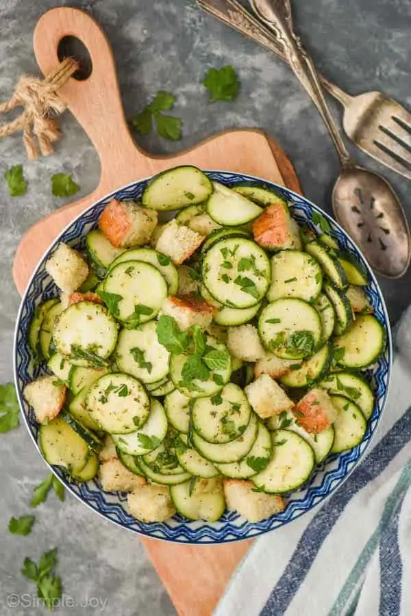 overhead view of a zucchini salad recipe in a bowl on a cutting board, salad is garnished with more fresh herbs