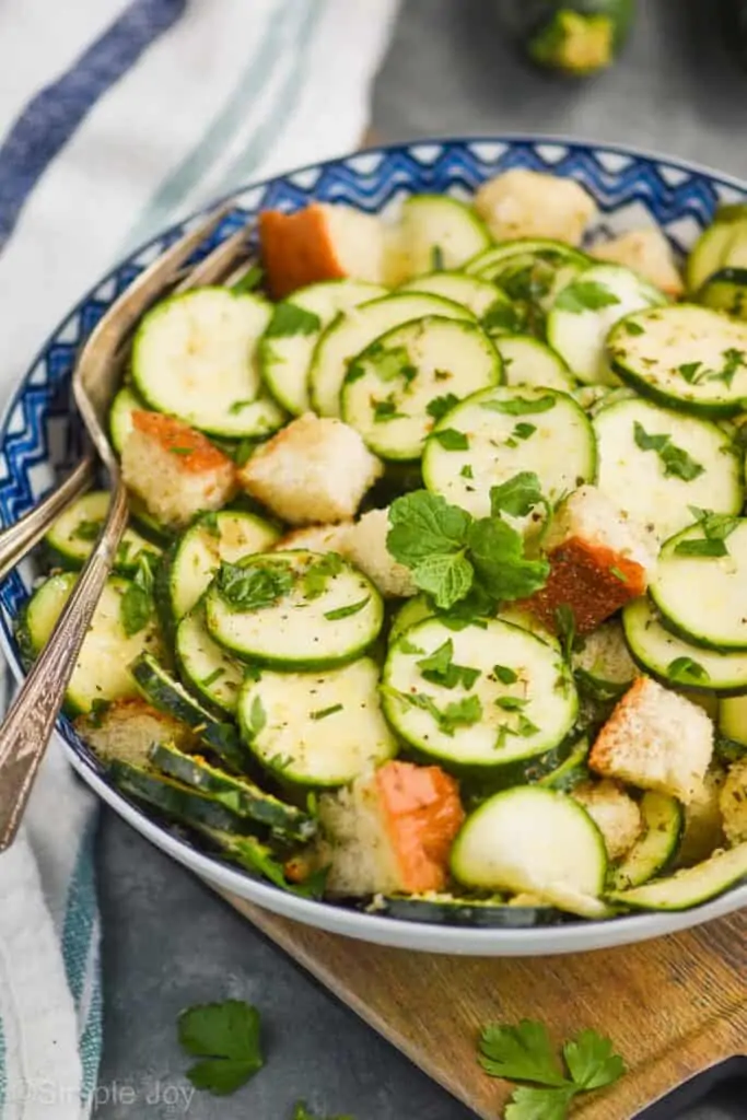 side view of zucchini panzanella salad in a bowl with fresh mint and parsley