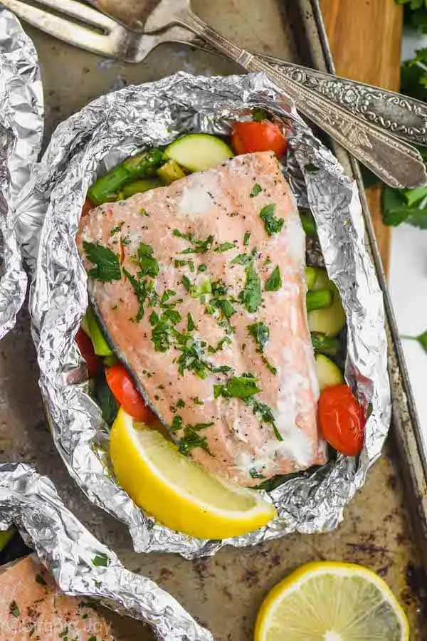 baked salmon in a foil packet garnished with flat leaf parsley and a fresh lemon wedge
