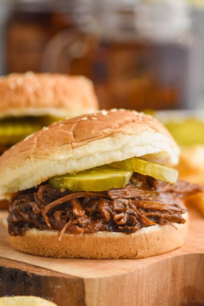 close up of bbq beef recipe on a sesame seed bun with two pickles on it