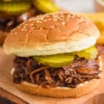 close up of bbq beef on a sesame seed bun with two pickles on it