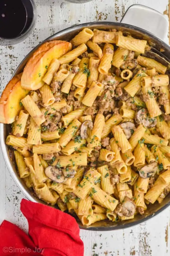 close up overhead of a skillet filled with beef and noodles recipe that has two pieces of garlic toast sticking out of it