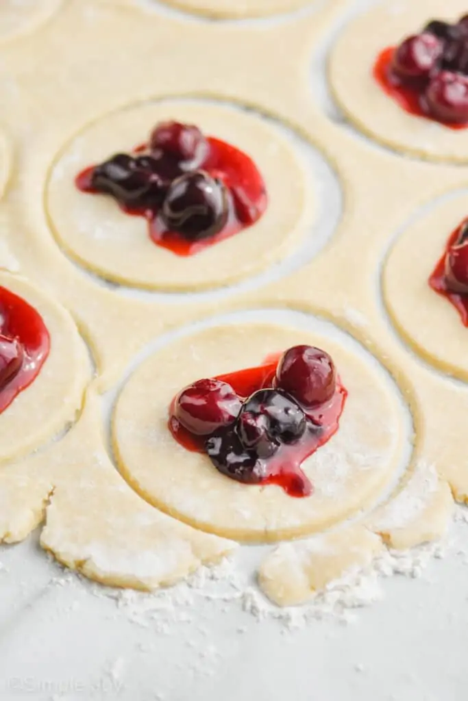 close up of cut circles of pie crust with cherry pie filling in the center of each one