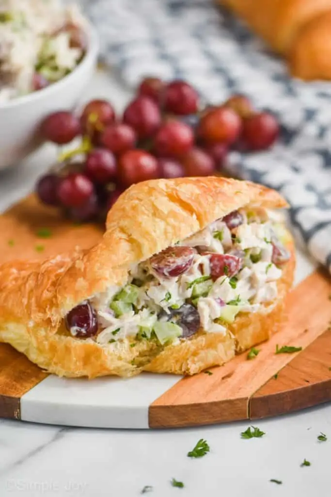 chicken salad sandwich on a croissant on a cutting board with grapes in the background