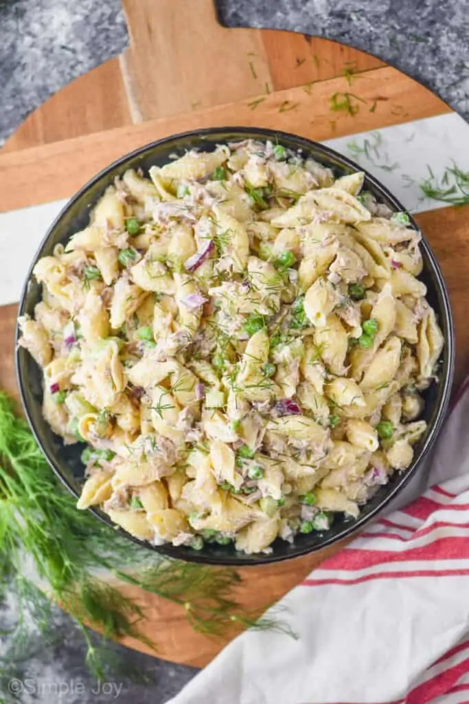 overhead photo of a serving bowl full of tuna pasta salad garnished with fresh dill with more fresh dill on the side