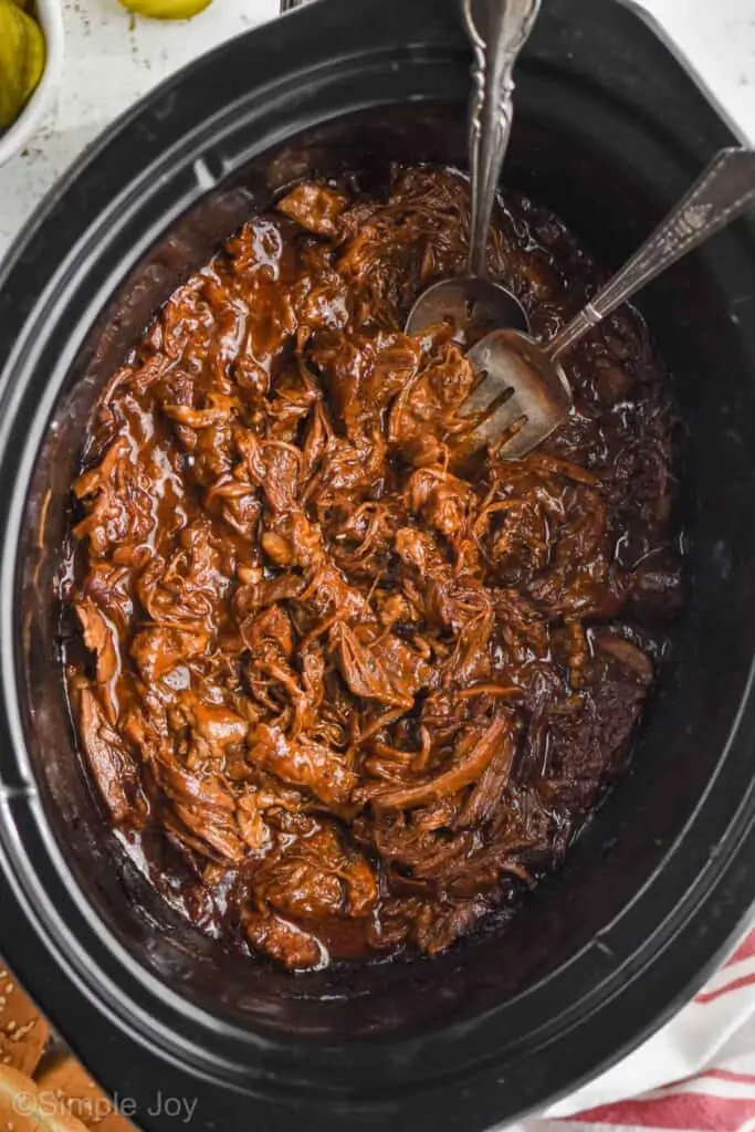 overhead of slow cooker bbq beef in a crockpot with a fork and spoon