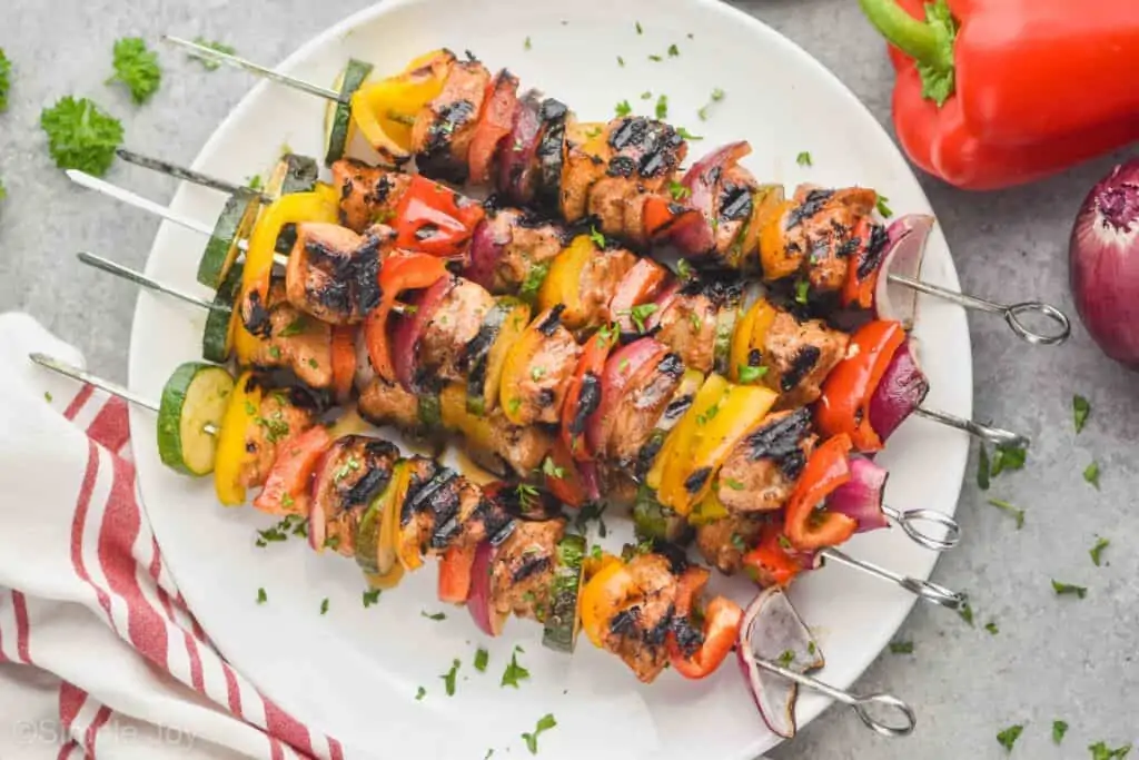 chicken kabobs that have been grilled and garnished with parsley, made with metal skewers on a white plate