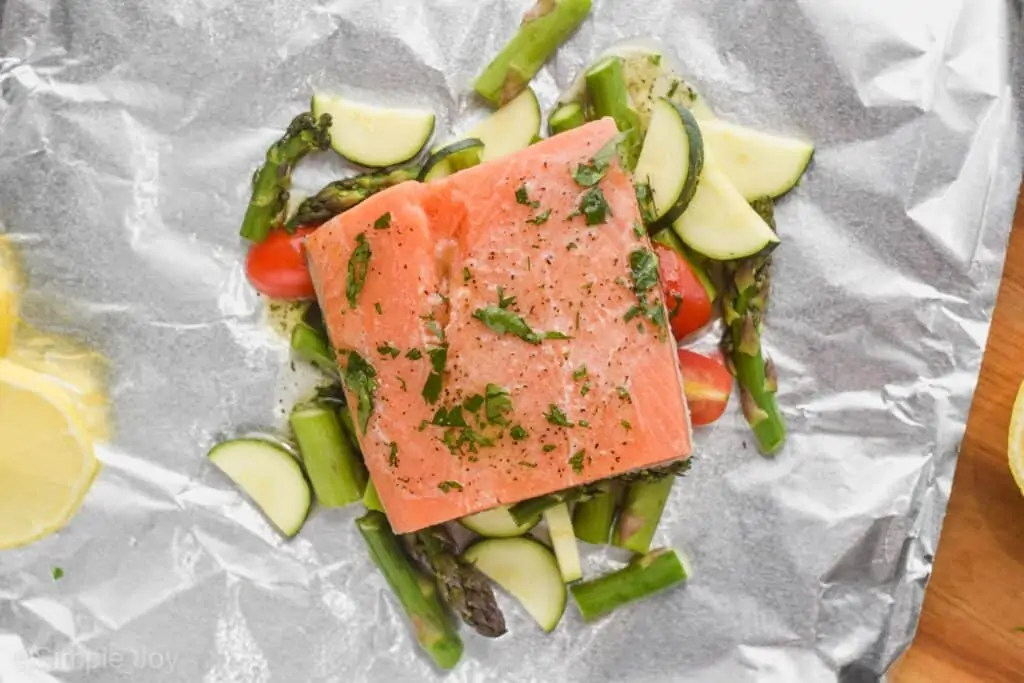 salmon prepared to be cooked in a foil packet with vegetables, toped with butter and parsley