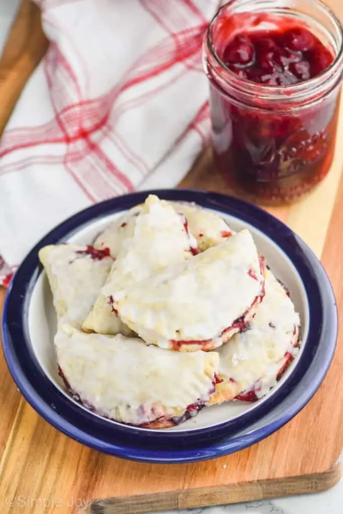 small plate of cherry hand pies piled on each other next to a mason jar filled with cherry pie filling