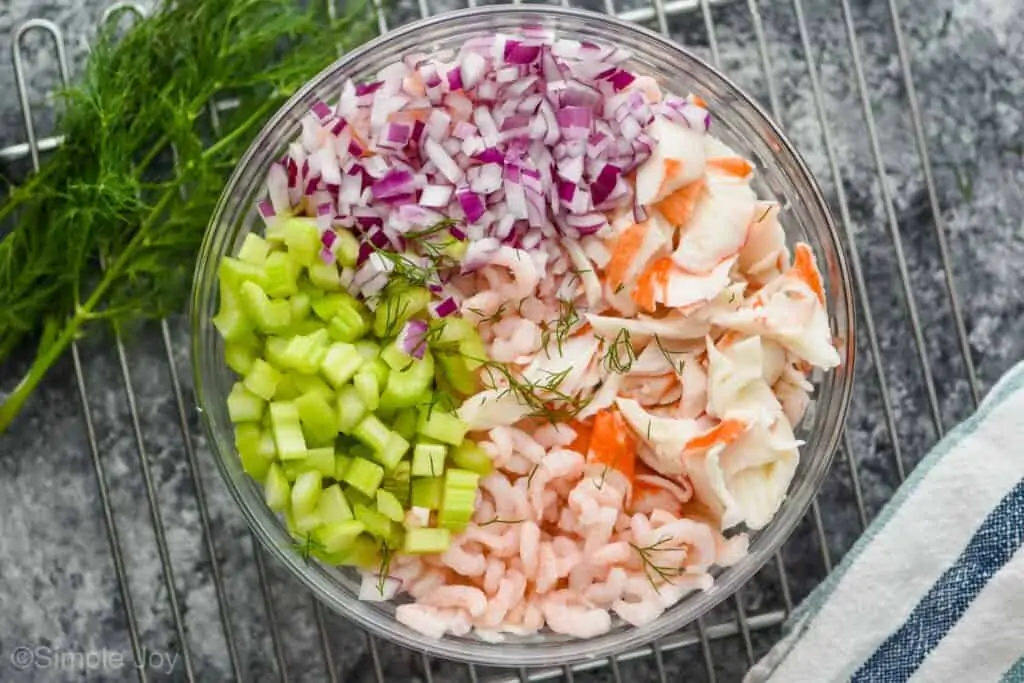 the ingredients for seafood salad separated by ingredient in a glass bowl, garnished with fresh dill