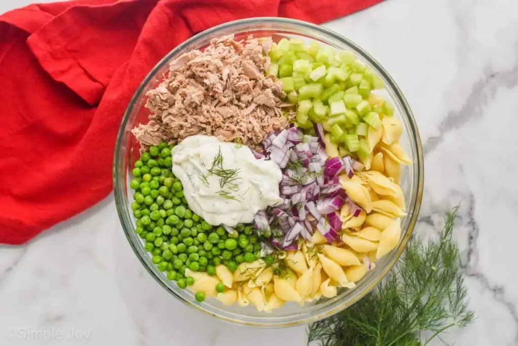 overhead photo of ingredients for tuna pasta salad broken up by ingredient in a glass bowl