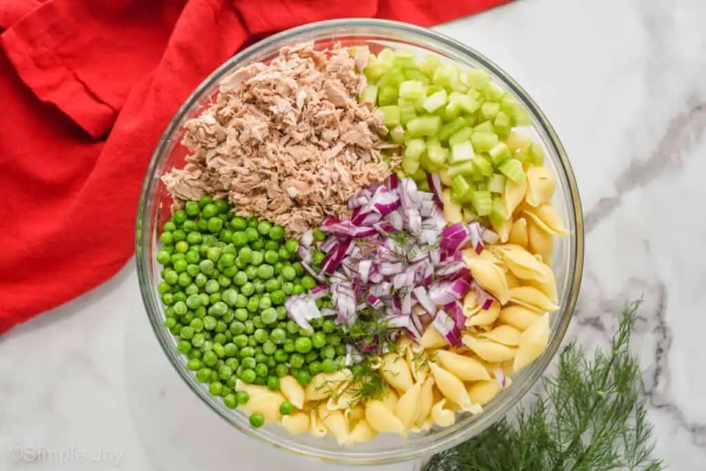 overhead photo of ingredients for tuna pasta salad broken up by ingredient in a glass bowl without the dressing
