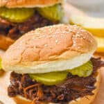 close up of bbq beef on a sesame seed bun with two pickles on it