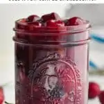 mason jar full of cherry pie filling with colander full of fresh cherries in the background
