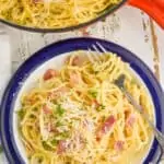 overhead view of a plate of pasta carbonara with a fork twirling the spaghetti, garnished with parmesan cheese and fresh parsley