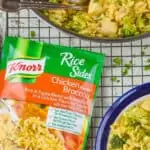 overhead view of a Knorr chicken broccoli rice side dish on a wire rack next to a skillet and a plate holding a chicken and broccoli rice casserole