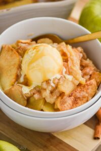 close up of an apple cobbler with vanilla ice cream on top and caramel sauce on that