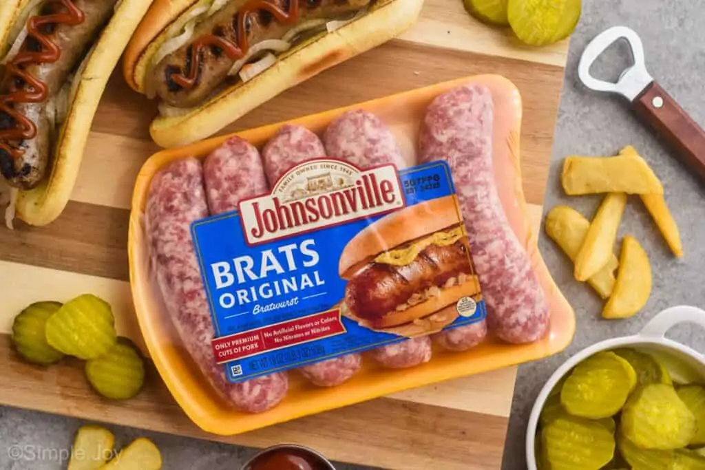 overhead of package of Johnsonville brats in the package on a cutting board surrounded by cooked beer brats