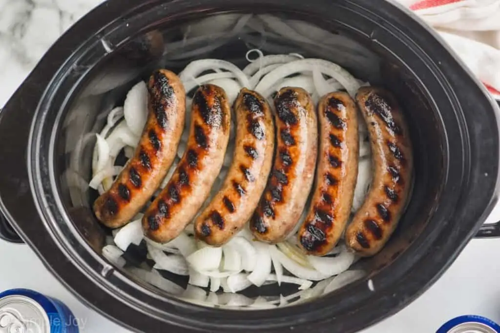 overhead of grilled brats a layer of onions in a slow cooker