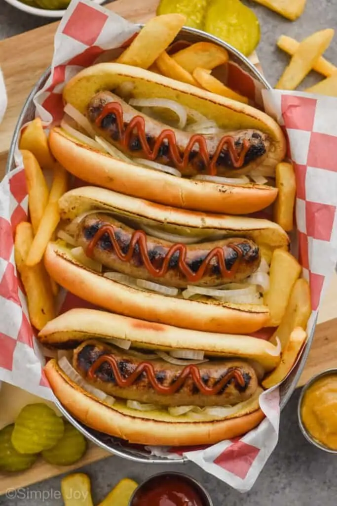 overhead of three beer brats in buns in a tray topped with ketchup