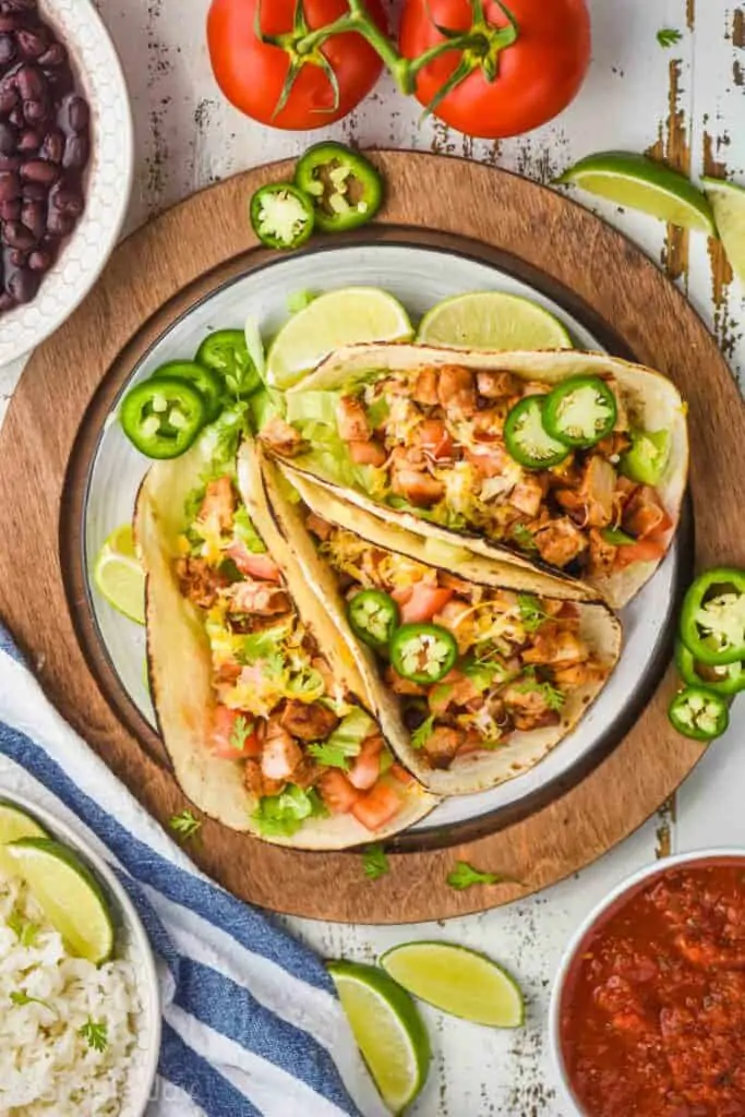 overhead view of three chicken tacos on a plate garnished with cilantro and fresh jalapeño slices