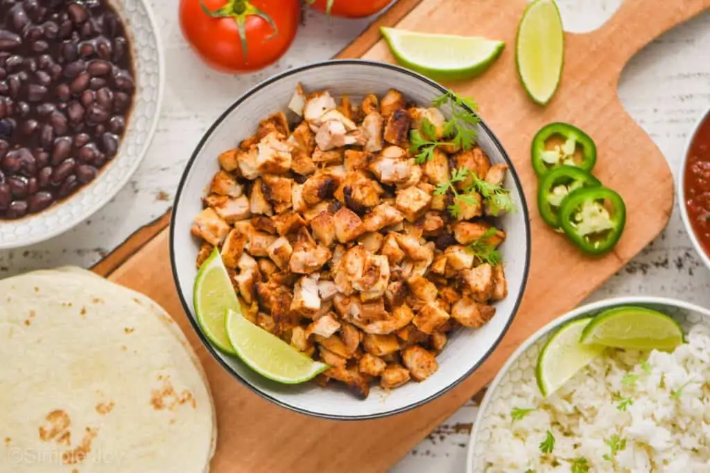 overhead view of a bowl of chicken taco meat with fresh cilantro on it and two lime wedges