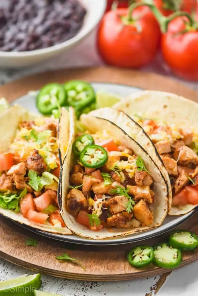 side view of three chicken tacos on a plate with fresh jalapeño slices, tomatoes, and lettuce