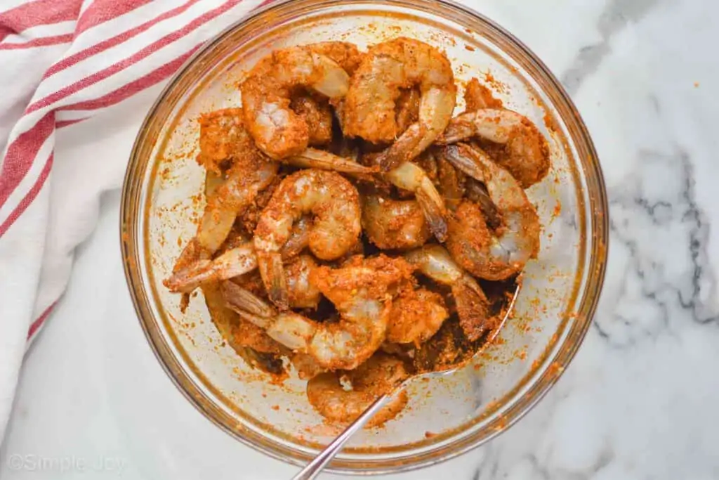 an overhead view of a mixing bowl full of raw shrimp covered in seasoning