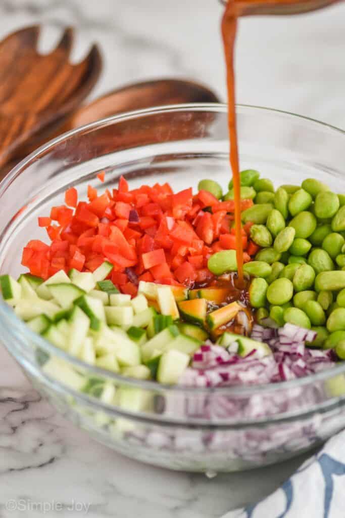 side view of edamame salad dressing being poured over the ingredients