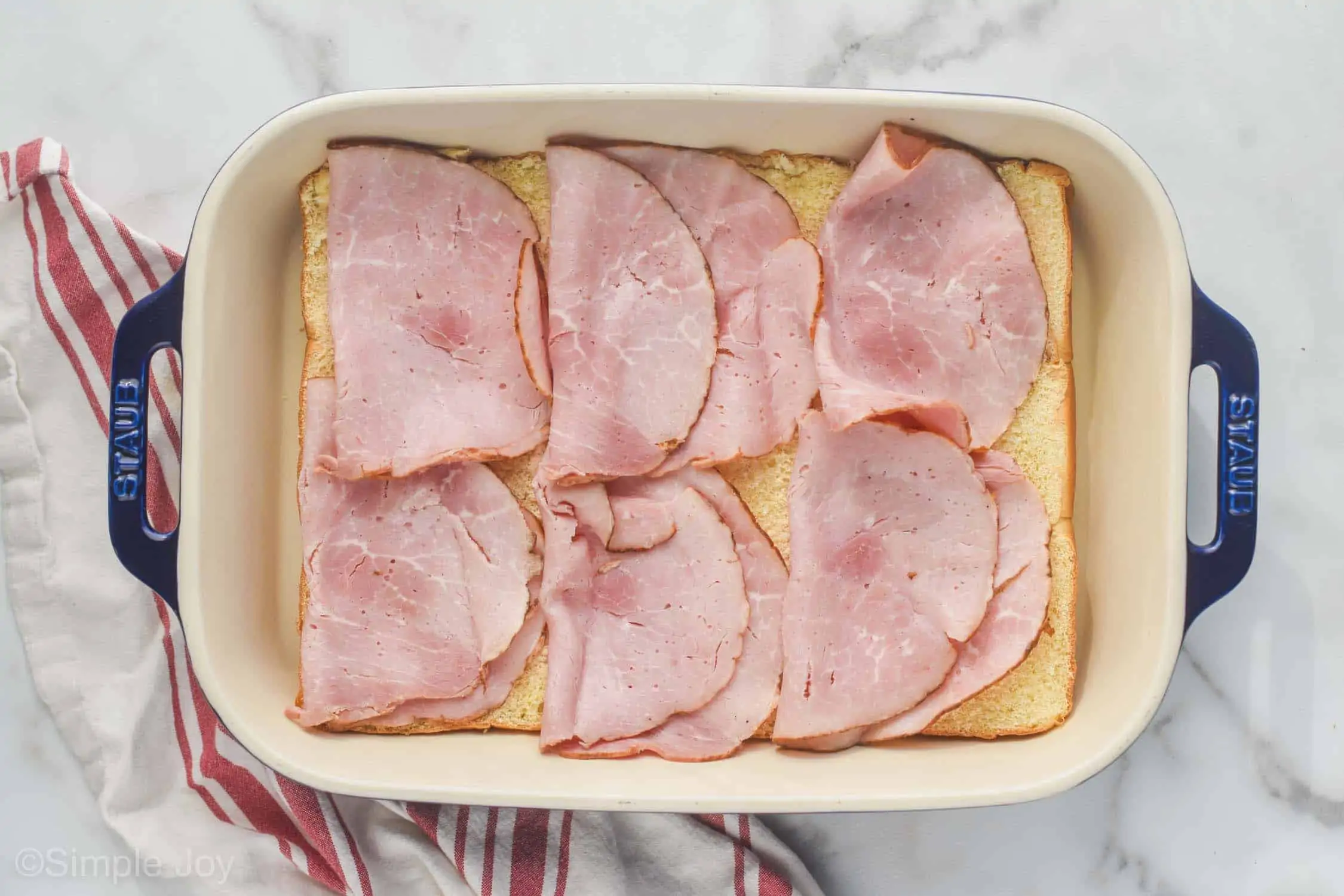 overhead of ham layered on the bottom of rolls to make ham and cheese sliders