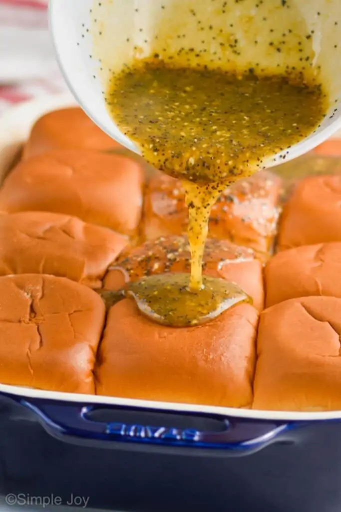 sauce being poured over ham and cheese sliders before baking