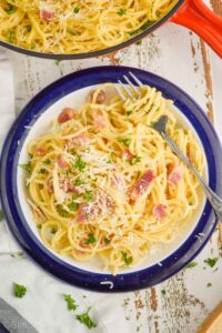 overhead view of a plate of pasta carbonara with a fork twirling the spaghetti, garnished with parmesan cheese and fresh parsley