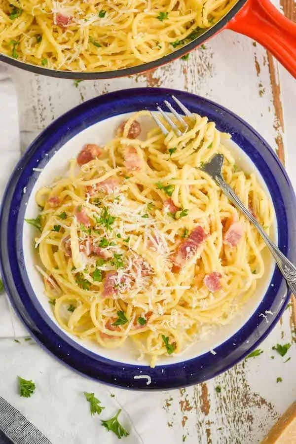 overhead view of a plate of pasta carbonara with a fork twirling the spaghetti, garnished with parmesan cheese and fresh parsley