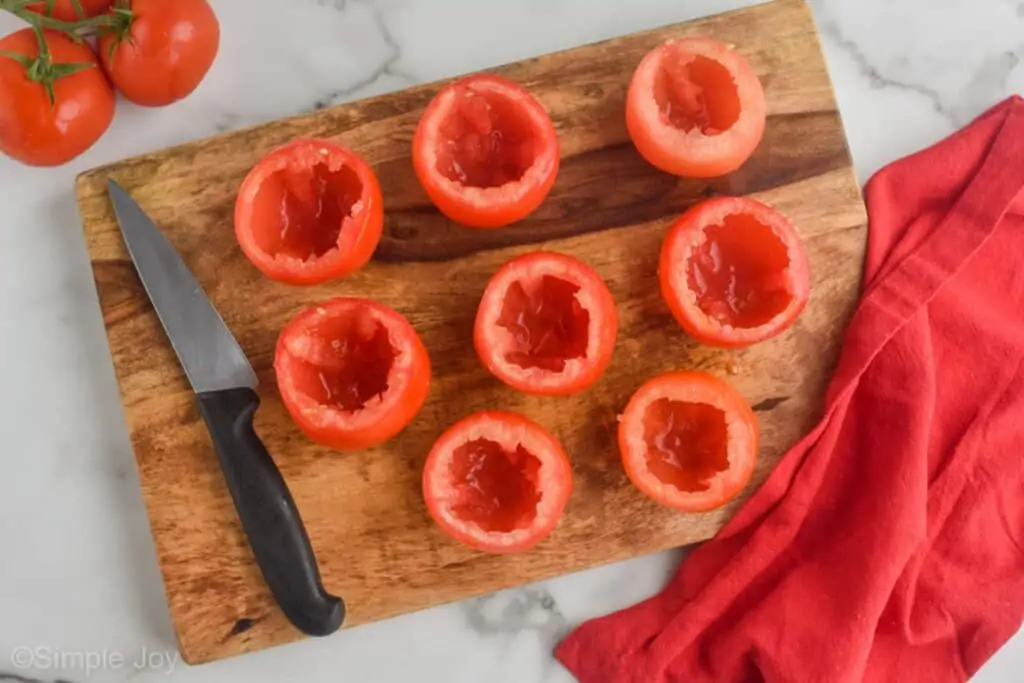 overhead photo of tomatoes that have been hallowed out sitting on a cutting board