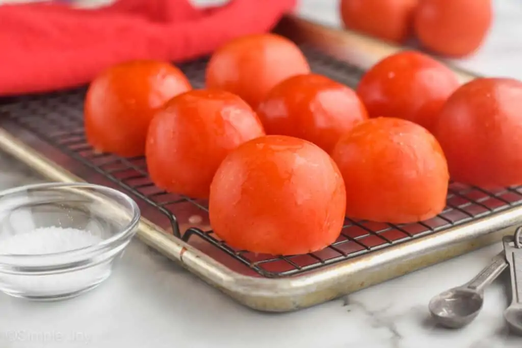 tomatoes that have had the tops removed upside down on a wire wrack that is inside of a rimmed baking sheet