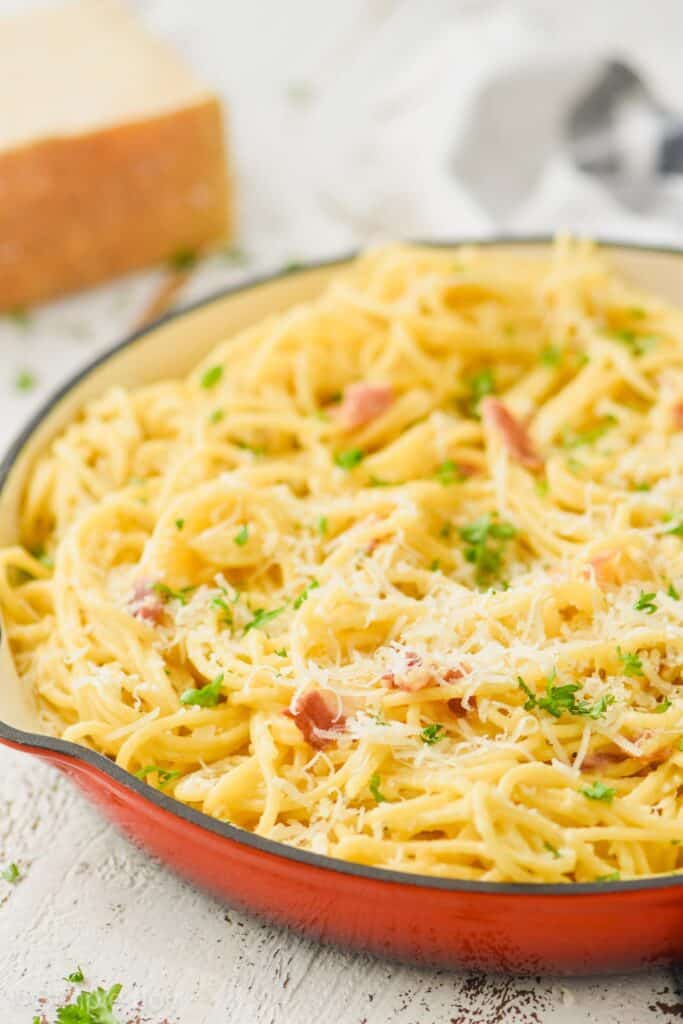 side view of pasta carbonara in skillet garnished with freshly grated parmesan cheese and parsley